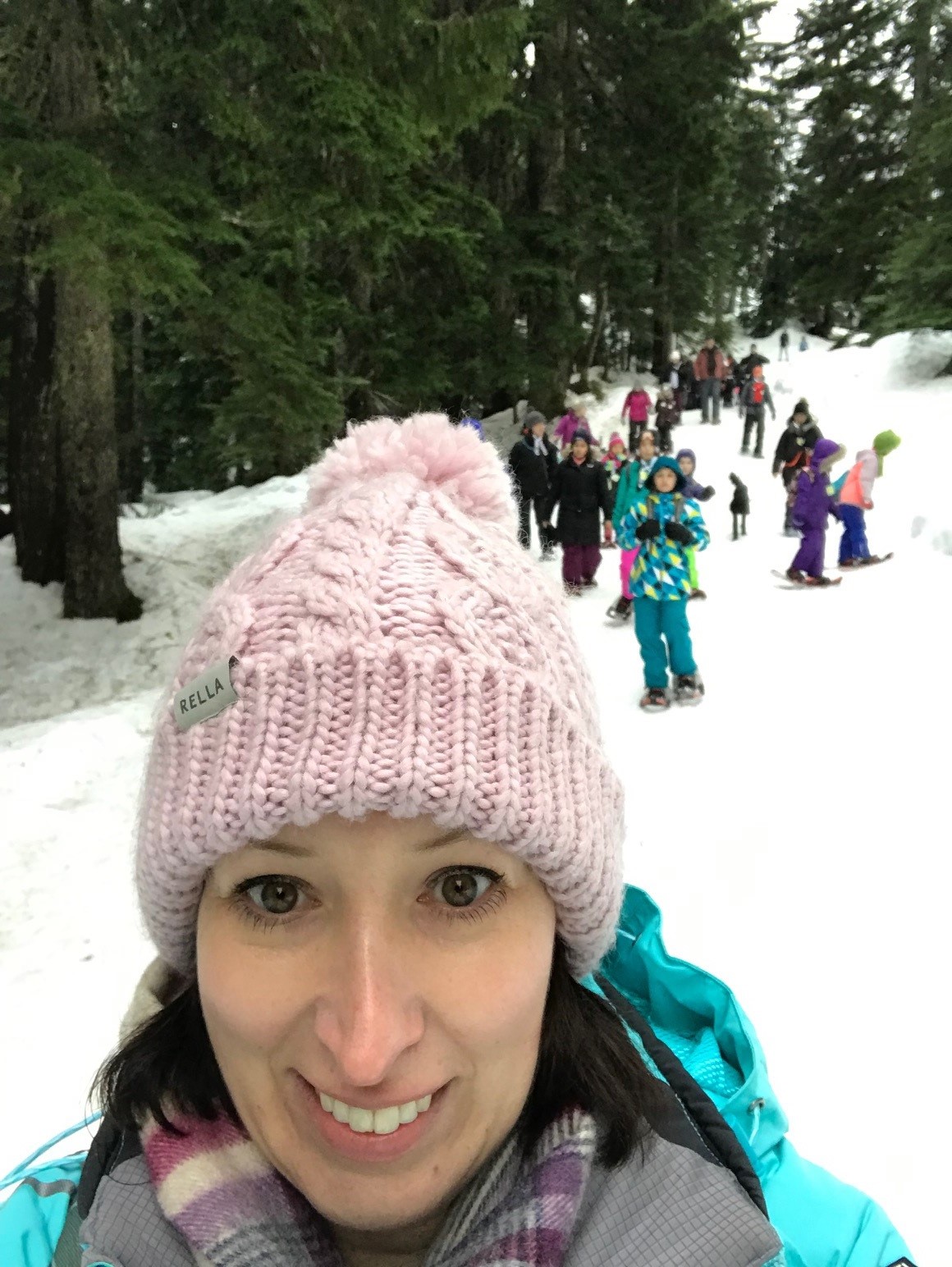 Femme prenant un selfie avec une toque rose. Il neige et il y a des enfants et des arbres derrière elle. Maxine Giannelli, directrice principale du développement et des communications d'Anxiété Canada.